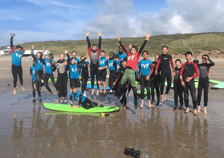 Year 8 pupils in wetsuits jumping as a group on beach in Wales