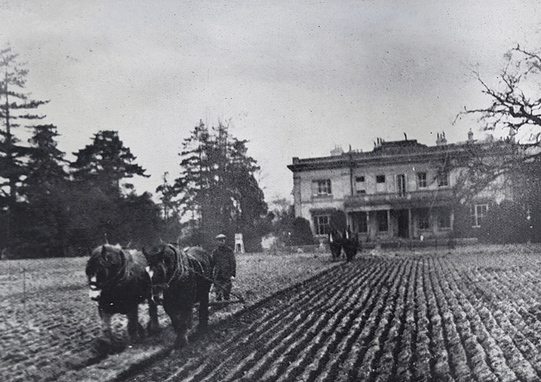Old black and white photo of horses pulling plough in front of the Leighton Park building