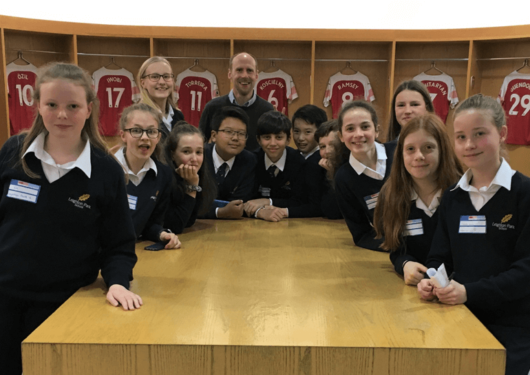 Group of young Leighton Park students around a table with football jerseys in the background
