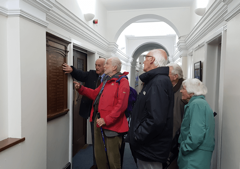 Old Leightonian Scrum Chums looking at wooden wall plaque for 70th anniverary