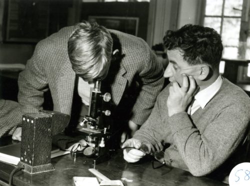 Old black and white photo of two men, one looking into a microscope
